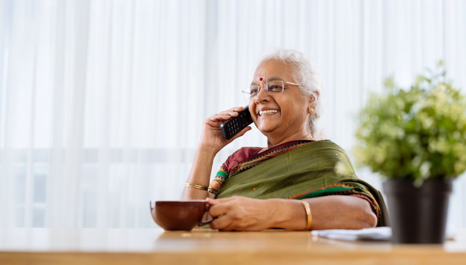 Senior woman smiling while on a phone call with a cup of tea
